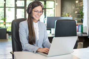 Young businesswoman with headset working on laptop in modern office