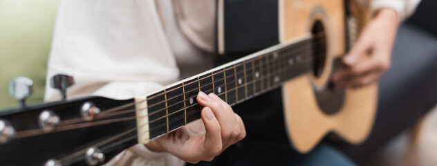 Obraz premium partial view of blurred woman playing guitar at home, banner.