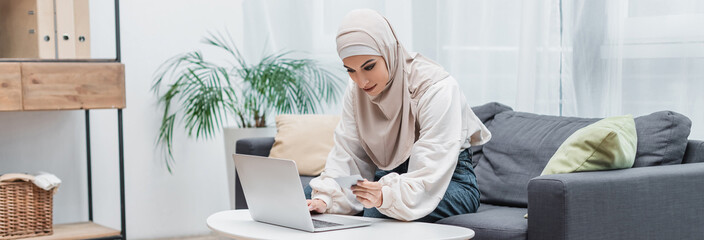 young muslim woman holding credit card during online shopping at home, banner.
