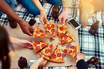 Pizza makes for the best picnics. Cropped shot of a group of friends eating pizza while having a...