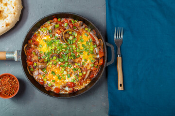 Shakshuka in a frying pan on a gray background next to a fork on a blue napkin.