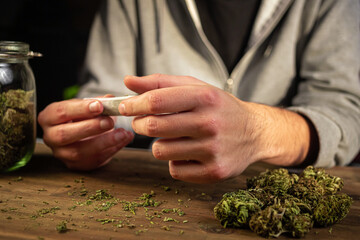 Man hands making a marijuana joint, rolling in a cigarette paper, a ground dried cannabis bud.