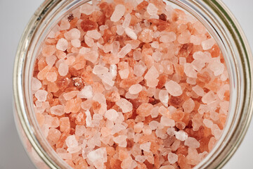 Fototapeta na wymiar Rose salt crystals in a glass container. Salty crystals in round glassware. Natural sea salt granules of chlorides. Himalayan spice for cooking and bathing. Colored rock salt. Chemical pink granules.
