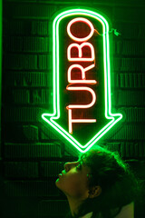 Beautiful young woman with curly hair near a green neon sign with the word "turbo".