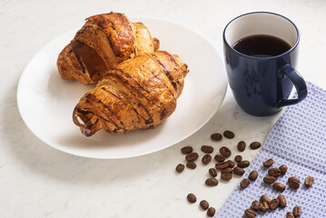 delicious, appetizing, crispy croissants, hot coffee in the blue cup and kitchen towel on plate on marble table