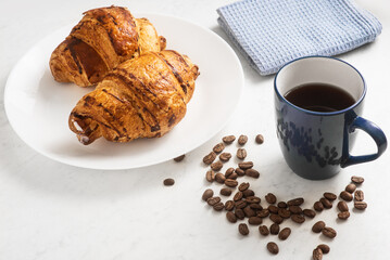 delicious, appetizing, crispy croissants, hot coffee in the blue cup and kitchen towel on plate on marble table