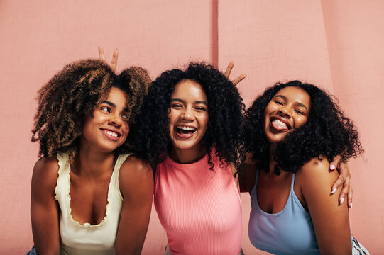 Portrait Of Three Laughing Females With Curly Hair. Happy Women Having Fun Together Looking At Camera.