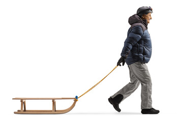 Full length profile shot of a mature man in winter clothes pulling a sled