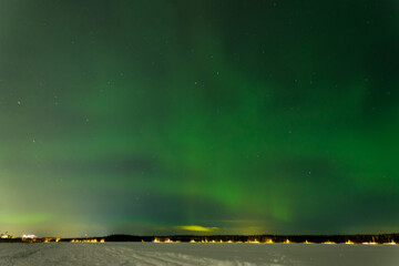 Green Northern Lights on the night sky with stars over snow
