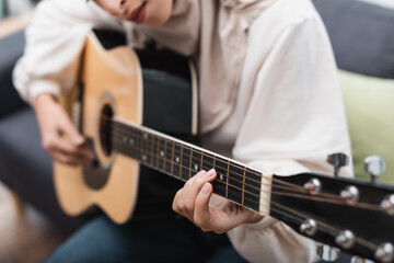 Fototapeta na wymiar cropped view of blurred muslim woman playing acoustic guitar at home.