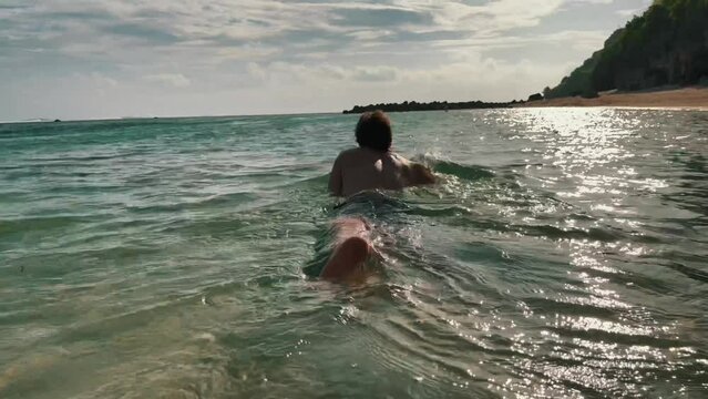 Anonymous man crawling and swimming at shallow sand beach in tropical paradise. Silhouette of happy male traveler in Bali island in Indonesia