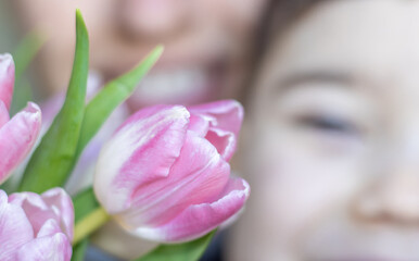 smiling woman with or without little son smiling in the back of pink tulip bouquet. photo with no focus, mom kissing the boy on cheek, thankful for flowers. mothers day concept. march 8