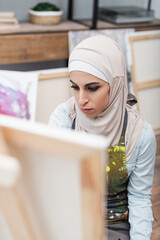 arabian woman in hijab drawing on blurred easel at home.