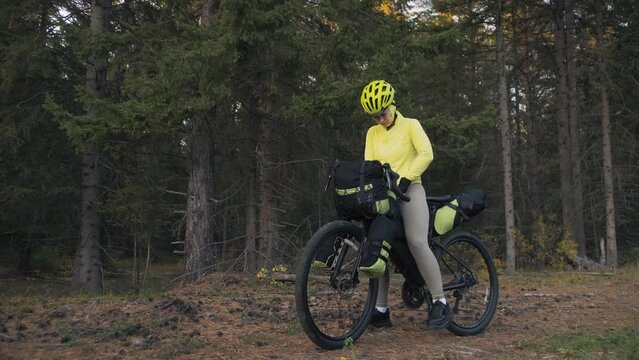 The woman travel on mixed terrain cycle touring with bike bikepacking outdoor. The traveler journey with bicycle bags. Stylish bikepacking, bike, sportswear in green black colors. Magic forest park.