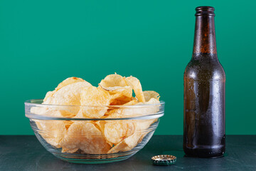 A bowl of chips and a beer over a green wood table