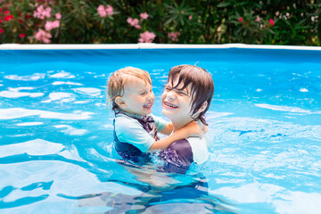 Two brothers of different age are playing in a swimming pool in summer during vacation. Happy...