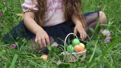 Little girl Wearing Bunny Ears collects a colorful egg in Garden. Easter hunting concept. Kid in spring meadow with Easter eggs hidden in the grass