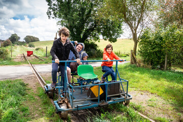 Family enjoying the rail bike attraction in France, Normandy. Father and sons on rail trolley. - obrazy, fototapety, plakaty
