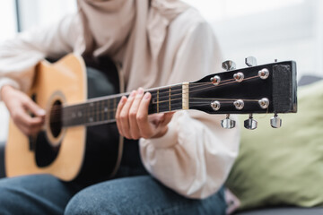 cropped view of blurred woman playing guitar while sitting at home.