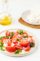 Fresh vegetable salad of tomatoes, red onion, feta cheese and basil herb and dressed with salt, pepper and virgine olive oil.