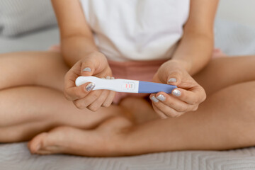 Closeup portrait of female hand holding positive pregnancy test while sitting on bed with crossed...