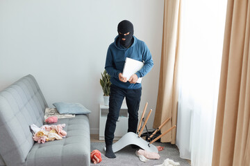 Dengerous man in a black mask and blue hoodie enters someone else's house to rob the owners,...