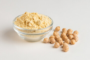 Chickpea flour in a glass bowl and chickpeas beans on a white background close up