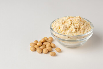Soy flour in a glass bowl and soybeans on a white background with copy space