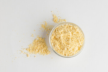Chickpea flour in glass bowl and scattered on white background, top view
