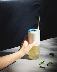 creamy long drink with basil and blue dust on a bar table 