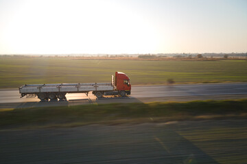 Aerial view of blurred fast moving semi-truck with cargo trailer driving on highway hauling goods in evening. Delivery transportation and logistics concept