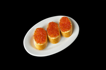 Red caviar on a piece of bread on a white plate isolated on a black background