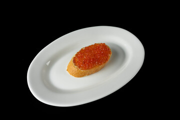 Red caviar on a piece of bread on a white plate isolated on a black background
