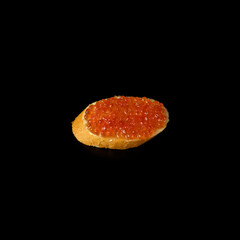 Red caviar on a piece of bread isolated on a black background