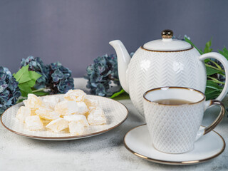 A teapot and a white mug on the table, flowers and traditional Turkish and Greek jelly candies in powdered sugar on a plate. confectionery in Arabic style..T The concept of recipes, 