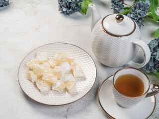 A teapot and a white mug on the table, flowers and traditional Turkish and Greek jelly candies in powdered sugar on a plate. confectionery in Arabic style..T The concept of recipes, 