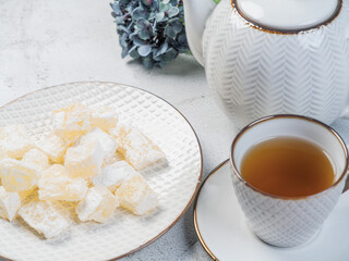 A teapot and a white mug on the table, flowers and traditional Turkish and Greek jelly candies in powdered sugar on a plate. confectionery in Arabic style..T The concept of recipes, 