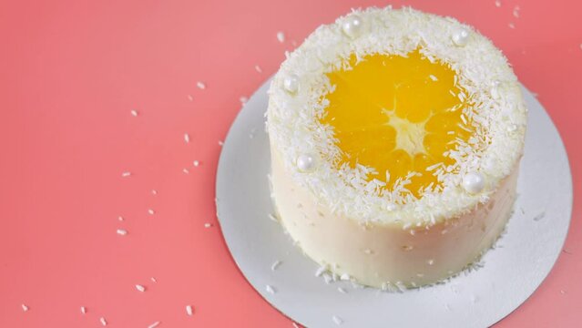 Cake with orange and coconut shavings spun on a pink background.