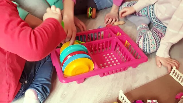 Little girls play children's kitchen and collect toy dishes in a drawer.