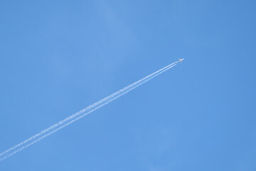 Distant passenger jet plane flying on high altitude on clear blue sky leaving white smoke trace of contrail behind. Air transportation concept