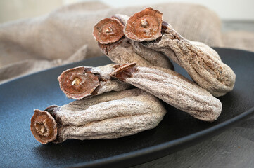 Dried textured large persimmon lies on a black plate. Persimmon is covered with powdered sugar. Close-up, selective focus. copy space