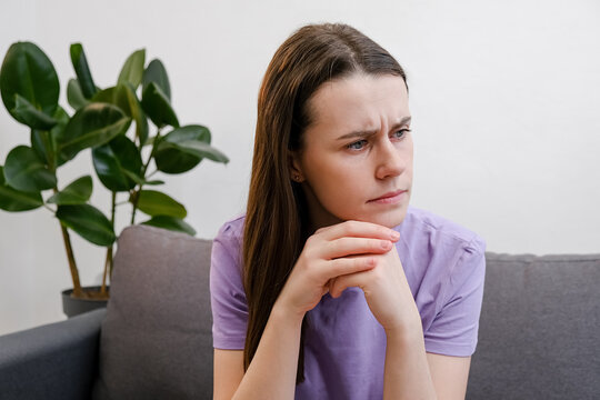 Pensive young woman 20s old years thinks of personal or relations problems, looks into distance feels thoughtful concerned sitting on sofa alone in living room. Life trouble considering, make decision