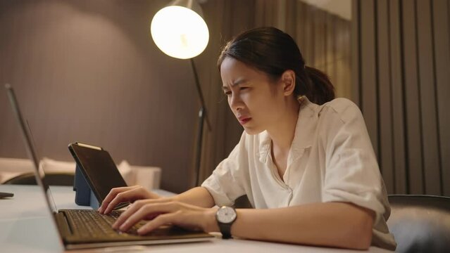 Asian female university student doing research and writing on her thesis until late night, rush work for upcoming due deadline, feeling exhausted and tiring, midnight study with laptop computer 