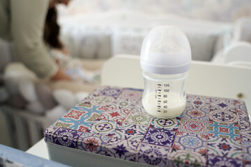 Milk in a bottle on the table. Mom takes care of a newborn baby.