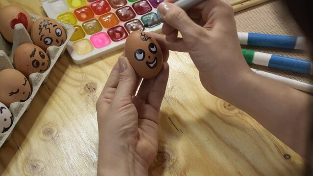 Easter decoration painted eggs with the image of a face. Drawing a face on an egg with a marker. Easter eggs drawing concept. Hands and egg clouse up.