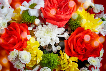 A bright background of a composition of flowers - daisies, chrysanthemums and red roses with light bokeh, close-up. Top view, flat lay