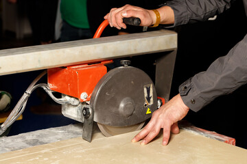 A worker cuts porcelain tiles on an industrial tile cutter with a diamond blade.