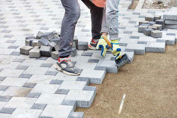 A worker in gloves lays paving slabs with a rubber mallet, observing the required pattern.