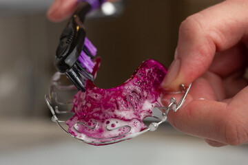 A woman is cleaning her removable Hawley retainer with a toothbrush. - obrazy, fototapety, plakaty