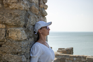 Close-up woman in a white blouse background of the defensive stone walls of the old fortress. She...